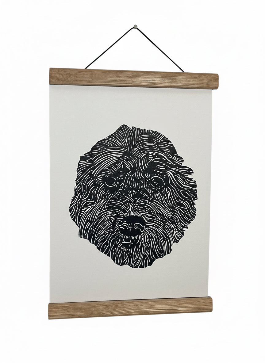 Black and white illustration of a dog's face on a white sheet of paper with a wooden frame, hanging on a light gray wall.